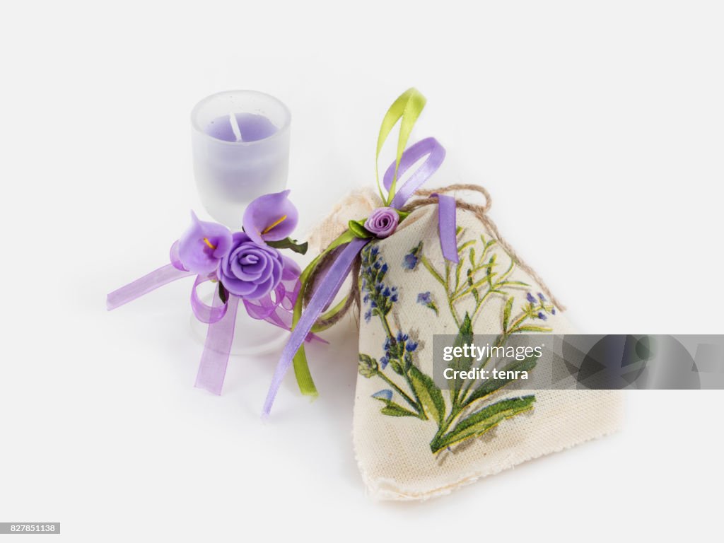 Handgemaakte linnen zak en aroma kaars in glas, versierd met kunstbloemen op witte achtergrond.