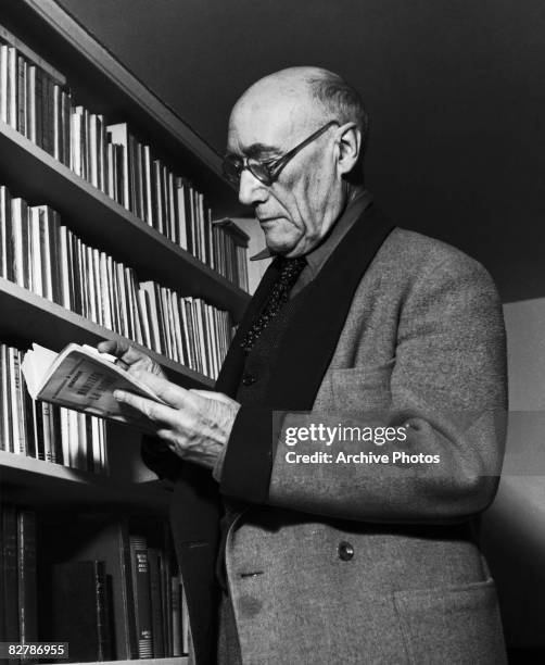 French author Andre Gide selects the novel 'Monsieur le Souris' by Georges Simenon at his Paris apartment, circa 1945.