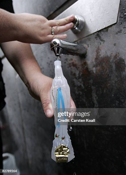 Young woman fills holy water in a bottle at a water tap beside the Statue of Our Lady of Lourdes at the entrance to the Grotto of Massabielle on...