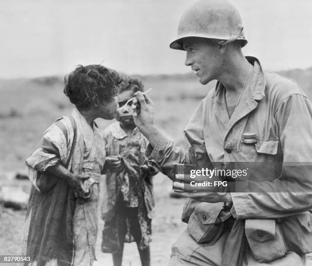 An American serviceman shares his rations with two Japanese children in Okinawa, Japan, 1945.