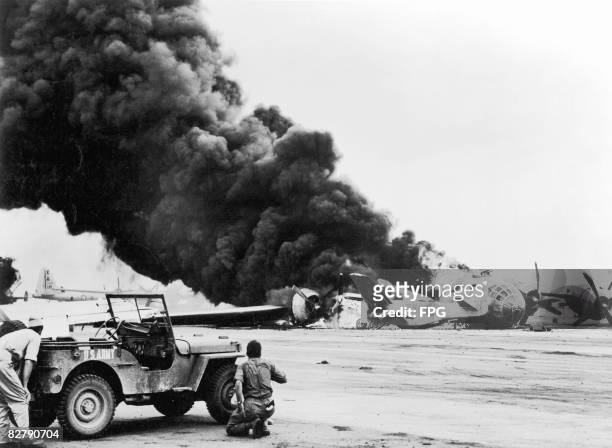 Servicemen shelter behind a jeep to avoid exploding ammunition as a B.29 Superfortress of the 21st Bomber Command crash-lands on Iwo Jima, colliding...