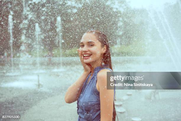 laughing young woman in wet clothes standing in water splashes of fountain - eastern european descent stock pictures, royalty-free photos & images