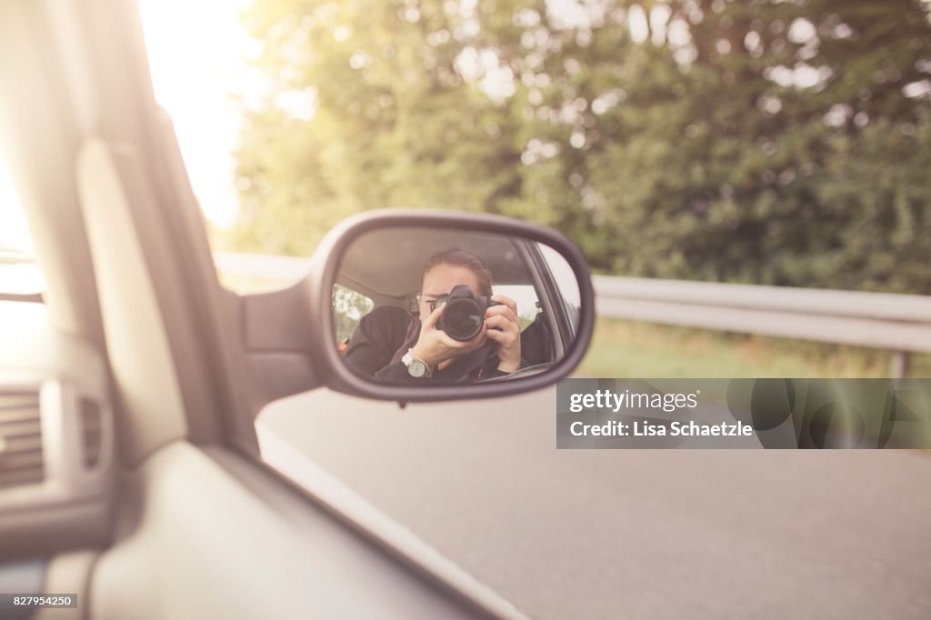Woman tourist taking photo in car with camera driving on road trip travel