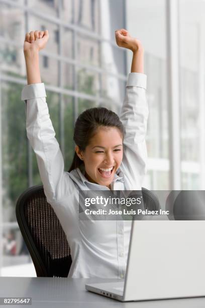 eurasian businesswoman on laptop celebrating in office - business woman cheering stockfoto's en -beelden