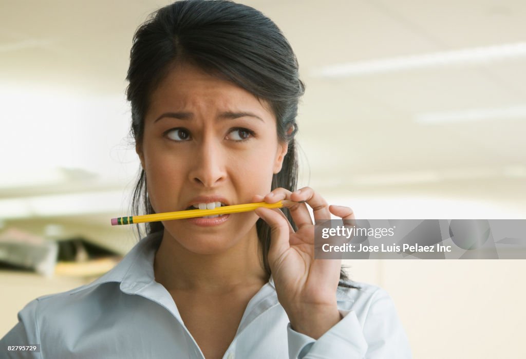 Eurasian businesswoman biting pencil looking worried