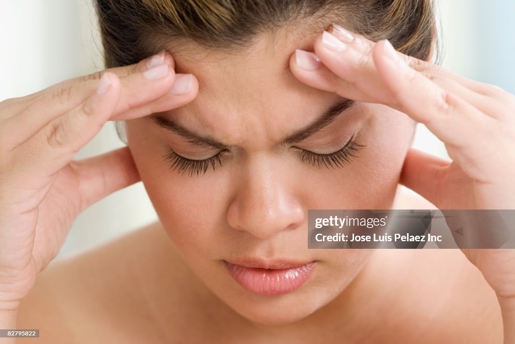 Hispanic woman holding forehead in pain