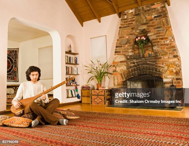 mixed race man playing sitar on living room floor - sittar stock pictures, royalty-free photos & images