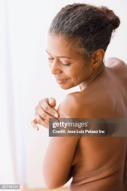 mixed race woman with bare chest applying lotion to arm - beautiful bare women photos et images de collection