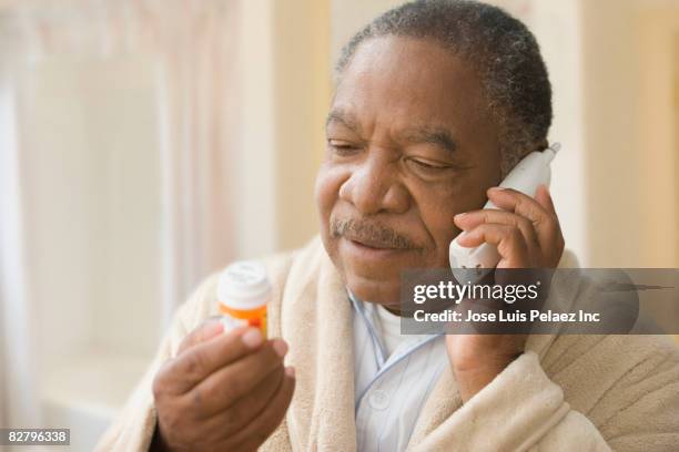 african man holding prescription bottle and talking on phone - prescription medicine bottle stock pictures, royalty-free photos & images