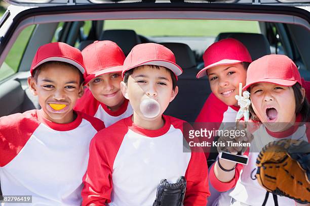 multi-ethnic boys in baseball uniforms making faces and holding trophy - baseballmannschaft stock-fotos und bilder