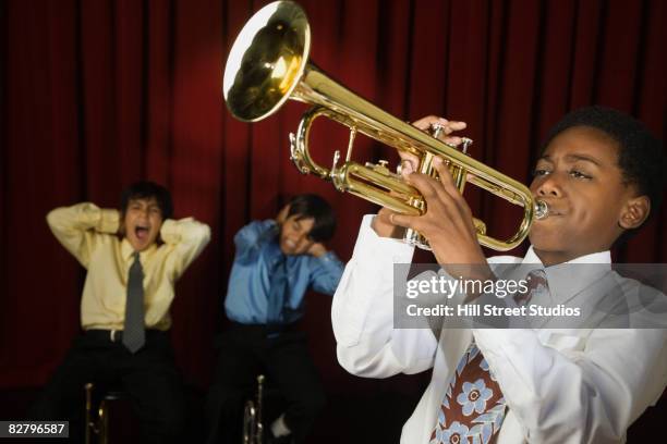 african boy playing trumpet with multi-ethnic classmates covering ears - terrible music stock pictures, royalty-free photos & images