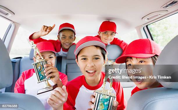 multi-ethnic boys in car wearing baseball uniforms and holding trophies - baseball strip fotografías e imágenes de stock