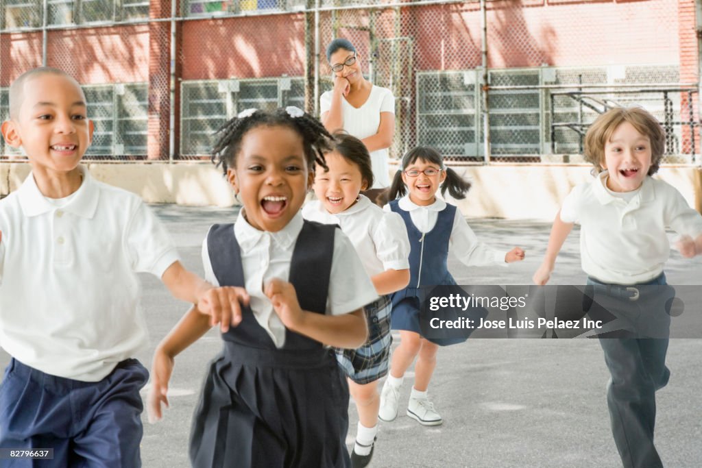 Multi-ethnic school children running from teacher outdoors