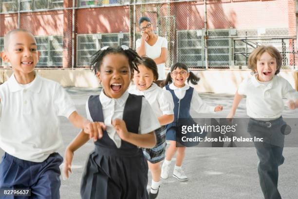 multi-ethnic school children running from teacher outdoors - uniform imagens e fotografias de stock