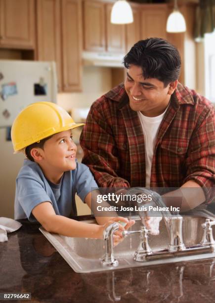 hispanic father and son wearing hard-hat washing hands in kitchen - boy in hard hat photos et images de collection