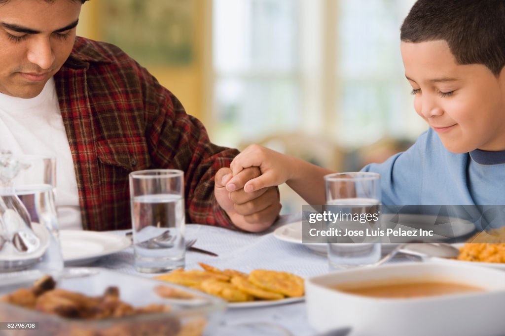 Hispanic father and son praying at dinner table