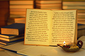 Open book illuminated by an oil lamp. Iliad opening lines.