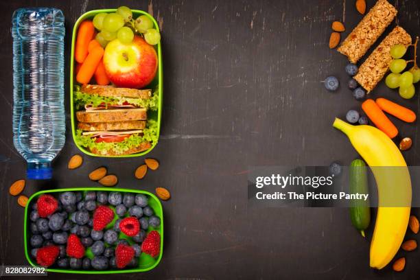 sandwich, apple, grape, carrot, berry in plastic lunch box and bottle of water on black chalkboard. back to school concept. - packed lunch - fotografias e filmes do acervo