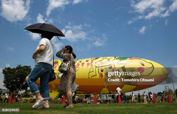 People walk past an airship with illustrations of Pikachu, a character from Pokemon series game titles, preparing to fly during the Pikachu Outbreak...
