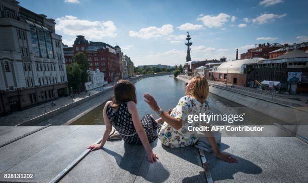 Women rest on a pedestrian bridge, with a giant statue of Peter the Great by Russian sculptor Zurab Tsereteli seen in the background, in Moscow on...