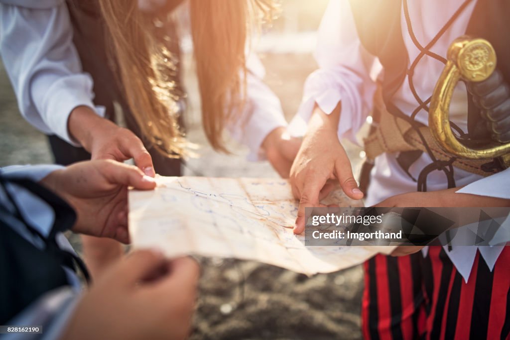 Kids pirates checking treasure map on a beach