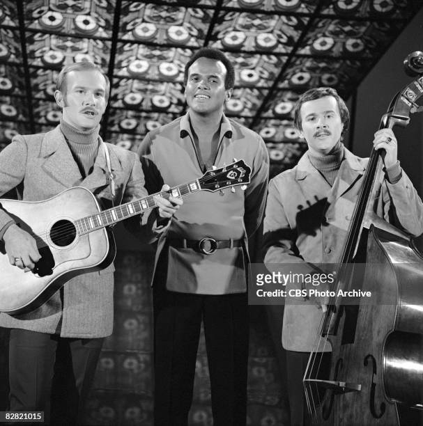Similarly dressed in blazers, turtleneck sweaters, and mustaches, American comedian musician brothers Tom Smothers and Dick Smothers stand on either...