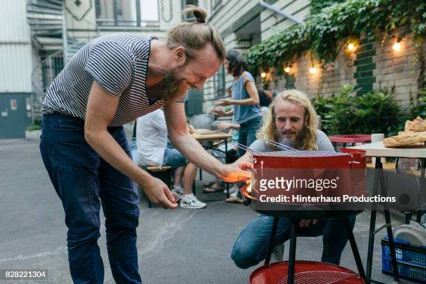 two young men lighting a barbecue, getting ready for dinner with friends"n - red hot summer party foto e immagini stock