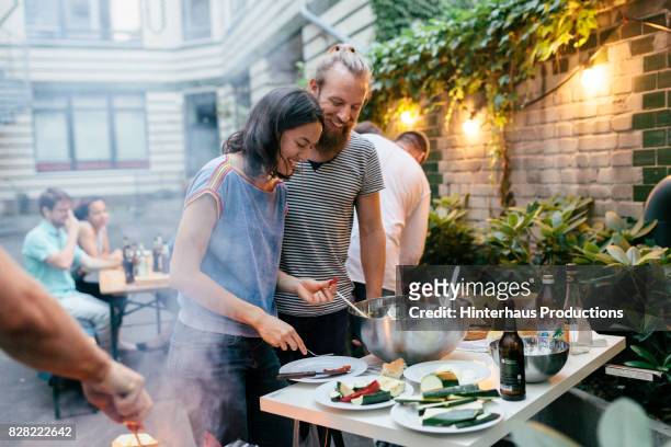 couple having barbecue with friends getting plates ready and preparing food - barbecue cibo foto e immagini stock