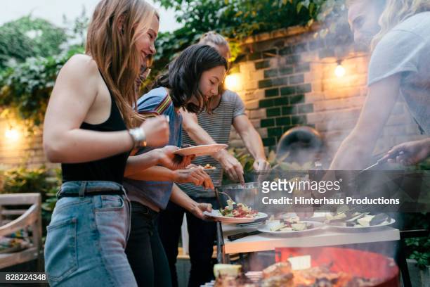 a group of friends helping themselves to food at a summer barbecue - barbecue social gathering stock pictures, royalty-free photos & images