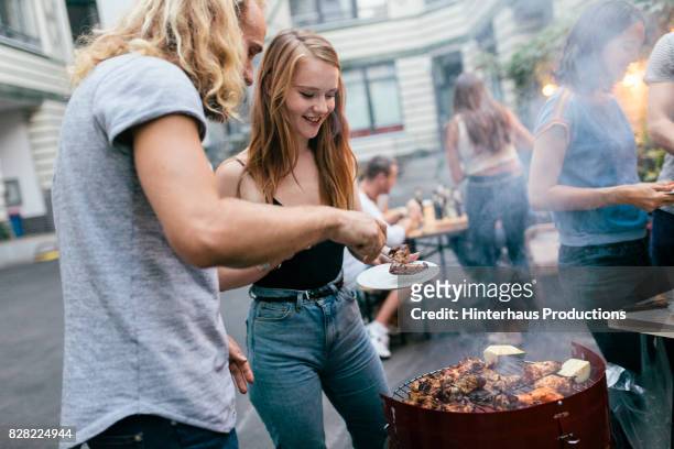 young man tending barbecue serving food to his friends"n - gartengrill stock-fotos und bilder