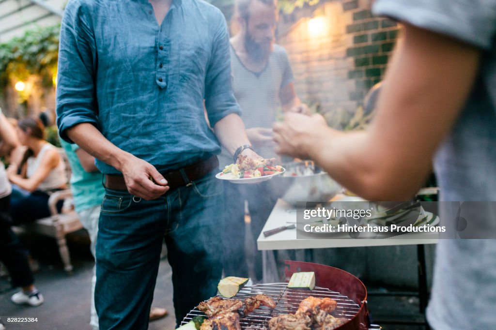 Group Of Friends Serving Food Straight From Barbecue At Evening Get Together