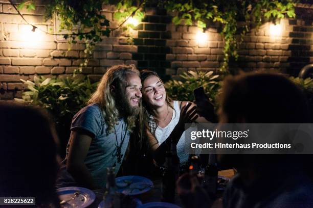 young couple looking at photos together after barbecue with friends - german greens party stockfoto's en -beelden