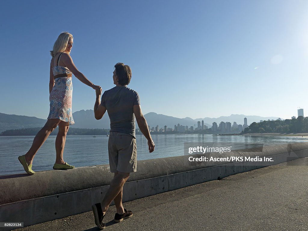 Couple hold hands while walking along waterfront