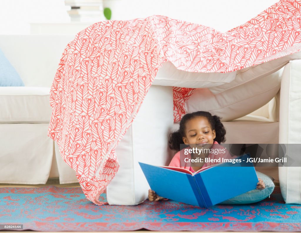 Mixed race girl reading in living room fort