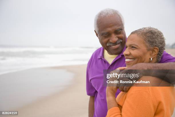 senior african couple hugging at beach - active seniors beach stock pictures, royalty-free photos & images