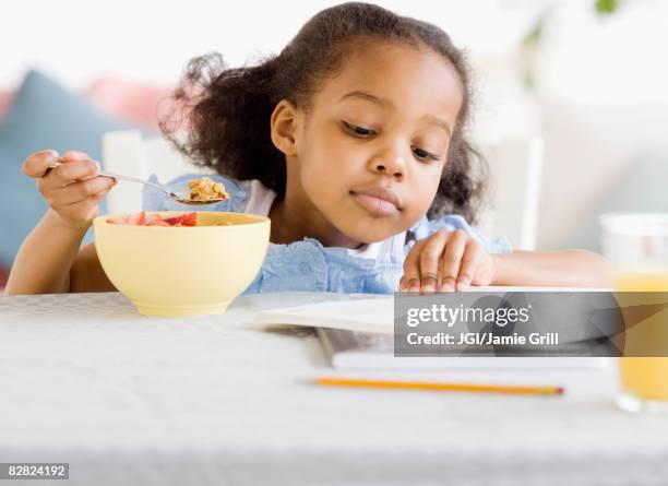 mixed race girl reading and eating breakfast - school breakfast stock pictures, royalty-free photos & images