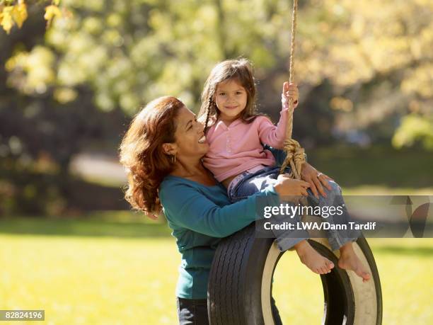 hispanic grandmother pushing granddaughter on tire swing - tire swing stock pictures, royalty-free photos & images