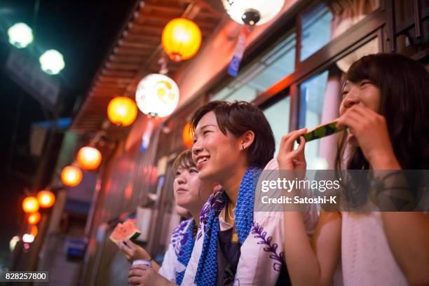 mulheres jovens, observando o desempenho de um festival local, comendo melancia - matsuri - fotografias e filmes do acervo