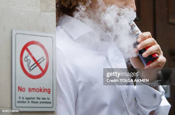 Smoker is engulfed by vapours as he smokes an electronic vaping machine during lunch time in central London on August 9, 2017. - World stock markets...