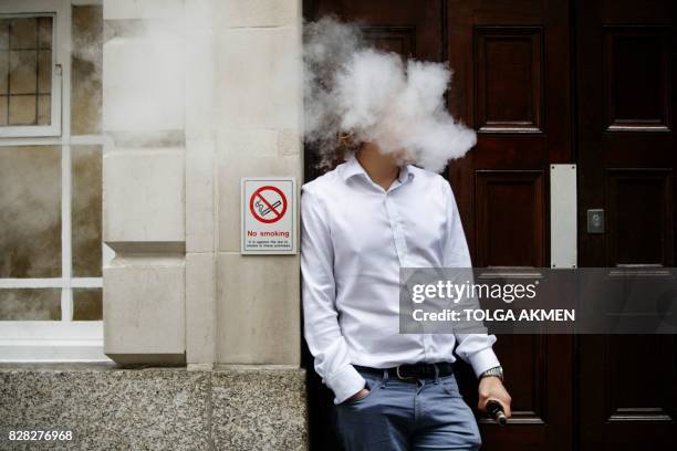 Smoker is engulfed by vapours as he smokes an electronic vaping machine during lunch time in central London on August 9, 2017. - World stock markets...