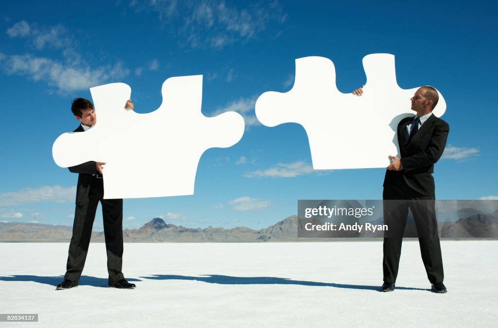 Businessmen holding Giant Puzzle Pieces in Desert.