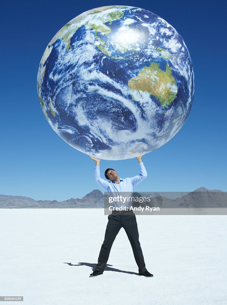 Man Holding up Globe in Desert
