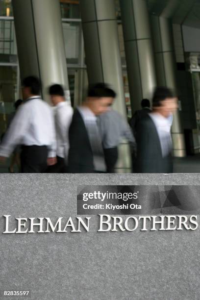 People walk past behind the sign of Lehman Brothers Holdings at the Tokyo branch of Lehman Brothers Holdings on September 16, 2008 in Tokyo, Japan....