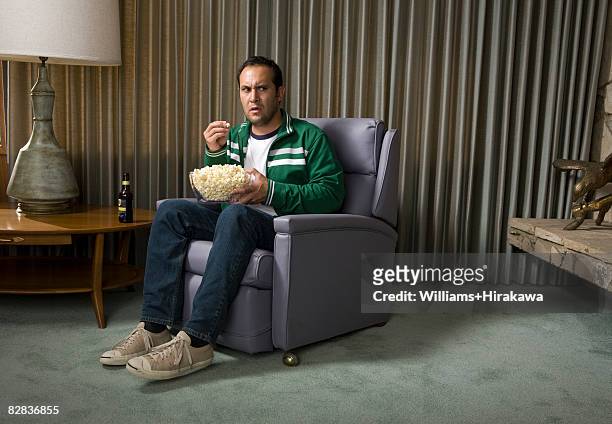man in chair eating popcorn - uncertainty stock-fotos und bilder