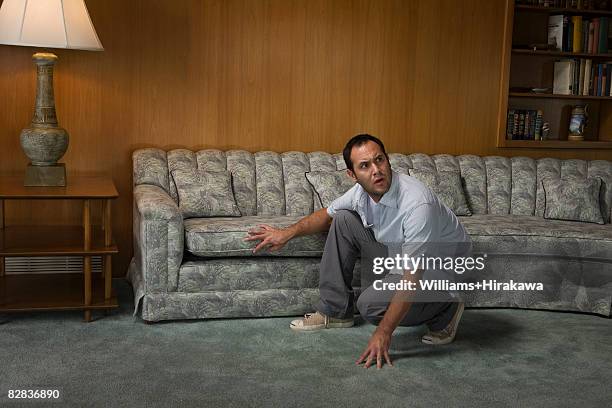 scared man crouching in front of sofa - look of fear man stockfoto's en -beelden