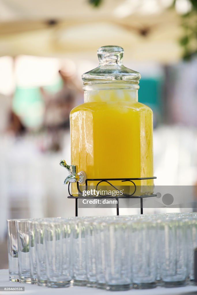 Big jar with lemonade and lot of glasses surrounded