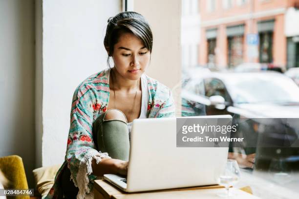 young woman working on laptop in cafe window - millennial generation stock pictures, royalty-free photos & images