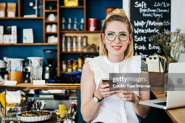 stylish young woman smiling using smartphone in cafe"n - blonde glasses stock-fotos und bilder