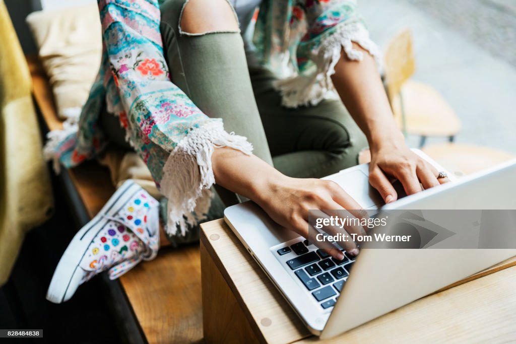 Close Up Of Young Woman Sat Down Using Laptop In Cafe