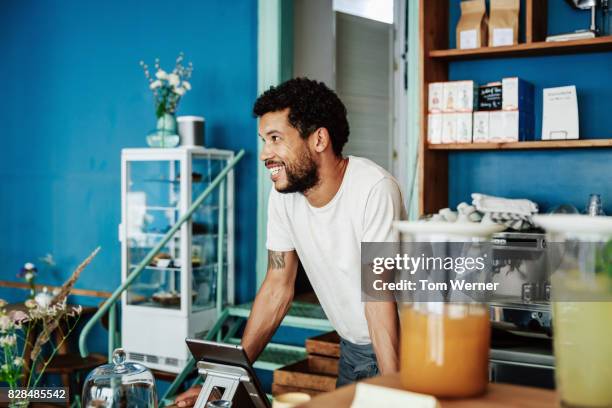 barista smiling as he chats with customers in coffee shop - barista photos et images de collection